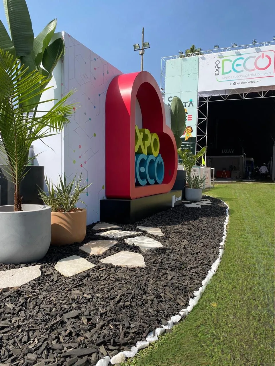 Letrero oficial EXPO DECO con jardín de mulch negro y borde de piedra blanca instalado por Samay